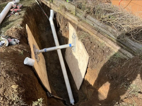 Open trench with a white PVC pipe and wooden braces during underground utility repair