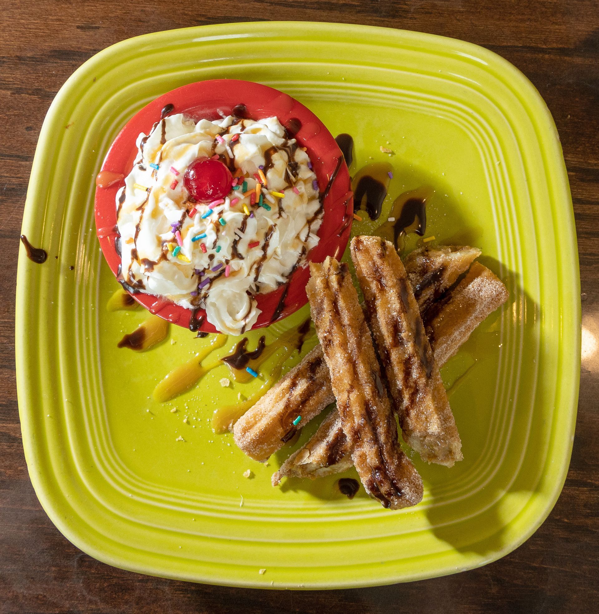 Churros with whipped cream, sprinkles, and syrup on a green plate.