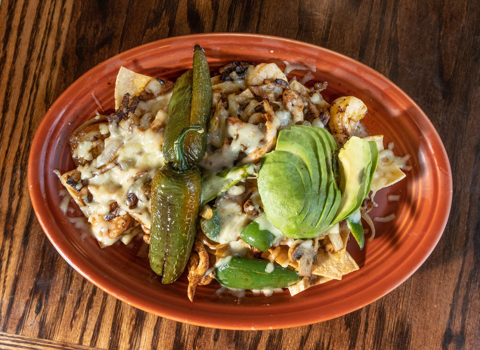 Nachos with cheese, avocado, and peppers on an orange plate on a wooden table.