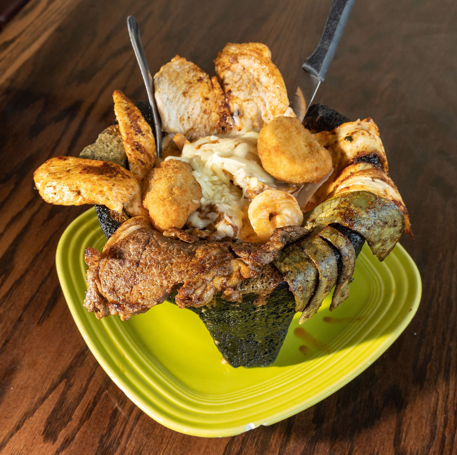 Grilled meat and fried foods piled high in a green bowl, on a wooden table.