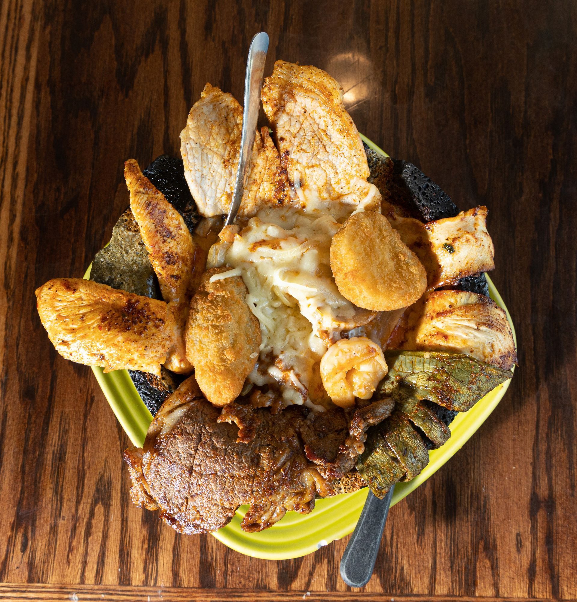 Plate of mixed grilled meats and fried foods, green plate on wood table.