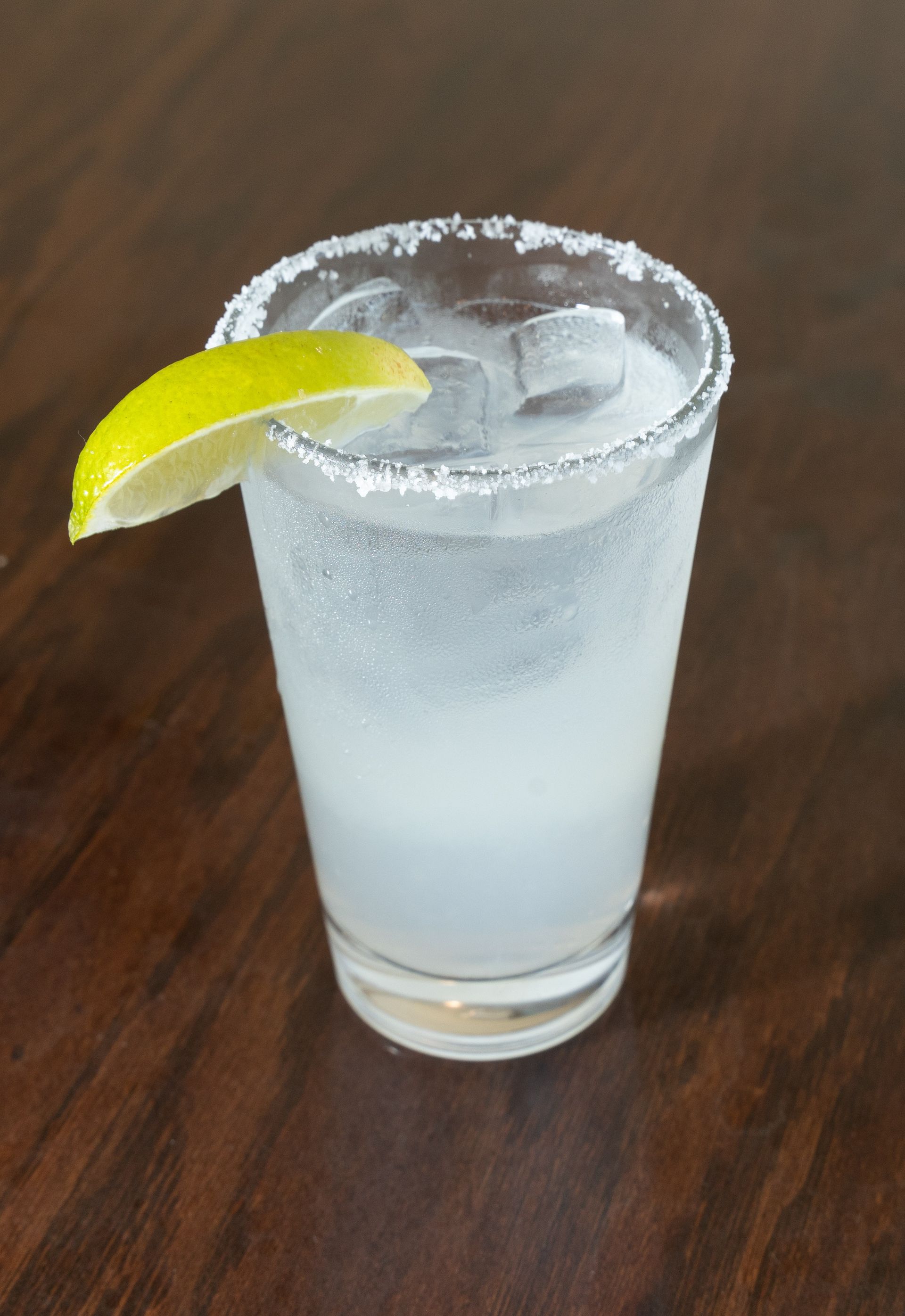 Cocktail with salt rim and lime garnish on wooden table.