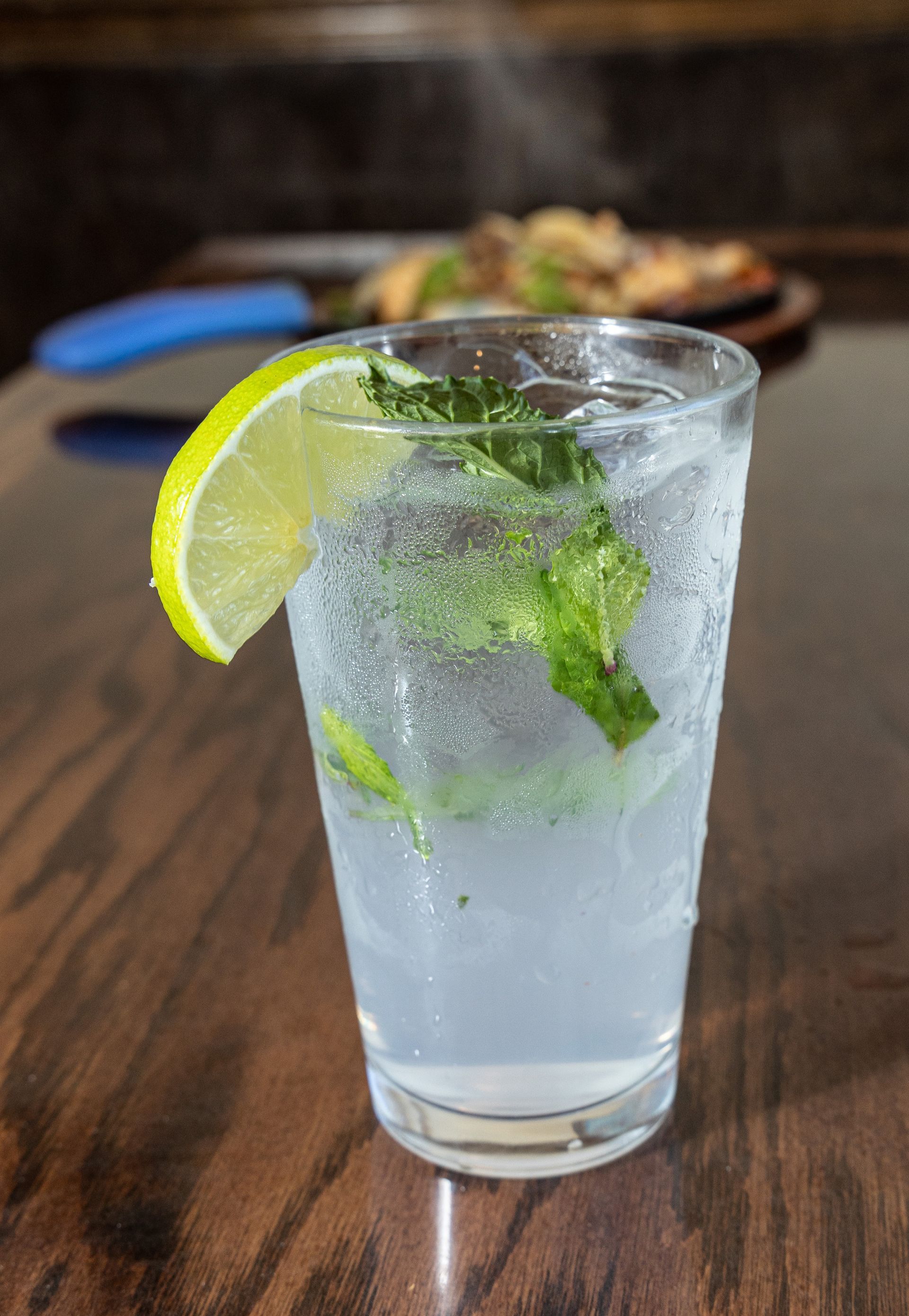 Mojito in a glass with a lime slice and mint, on a wooden table.