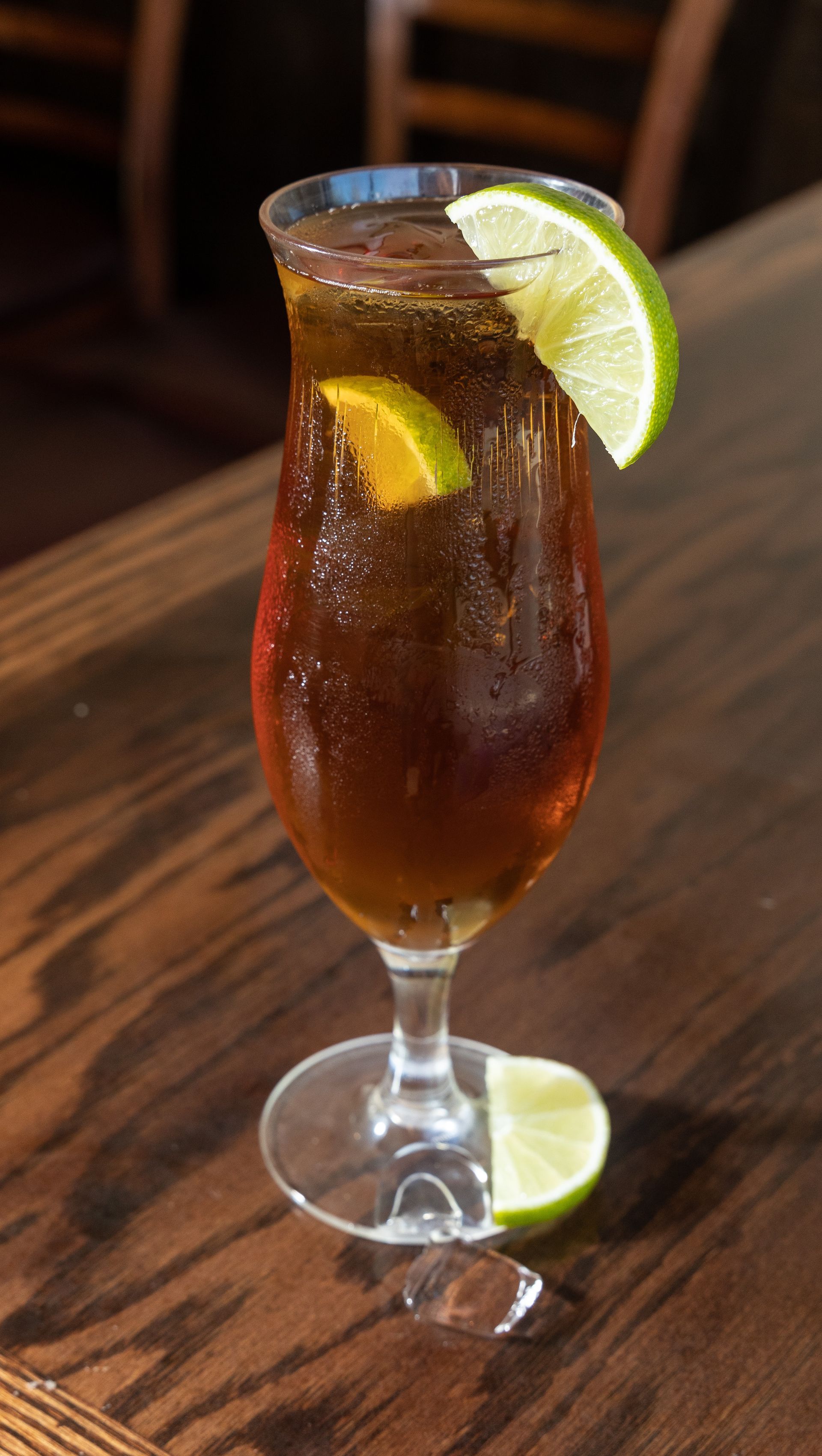 Cocktail in a stemmed glass with lime garnish, set on a wooden bar.