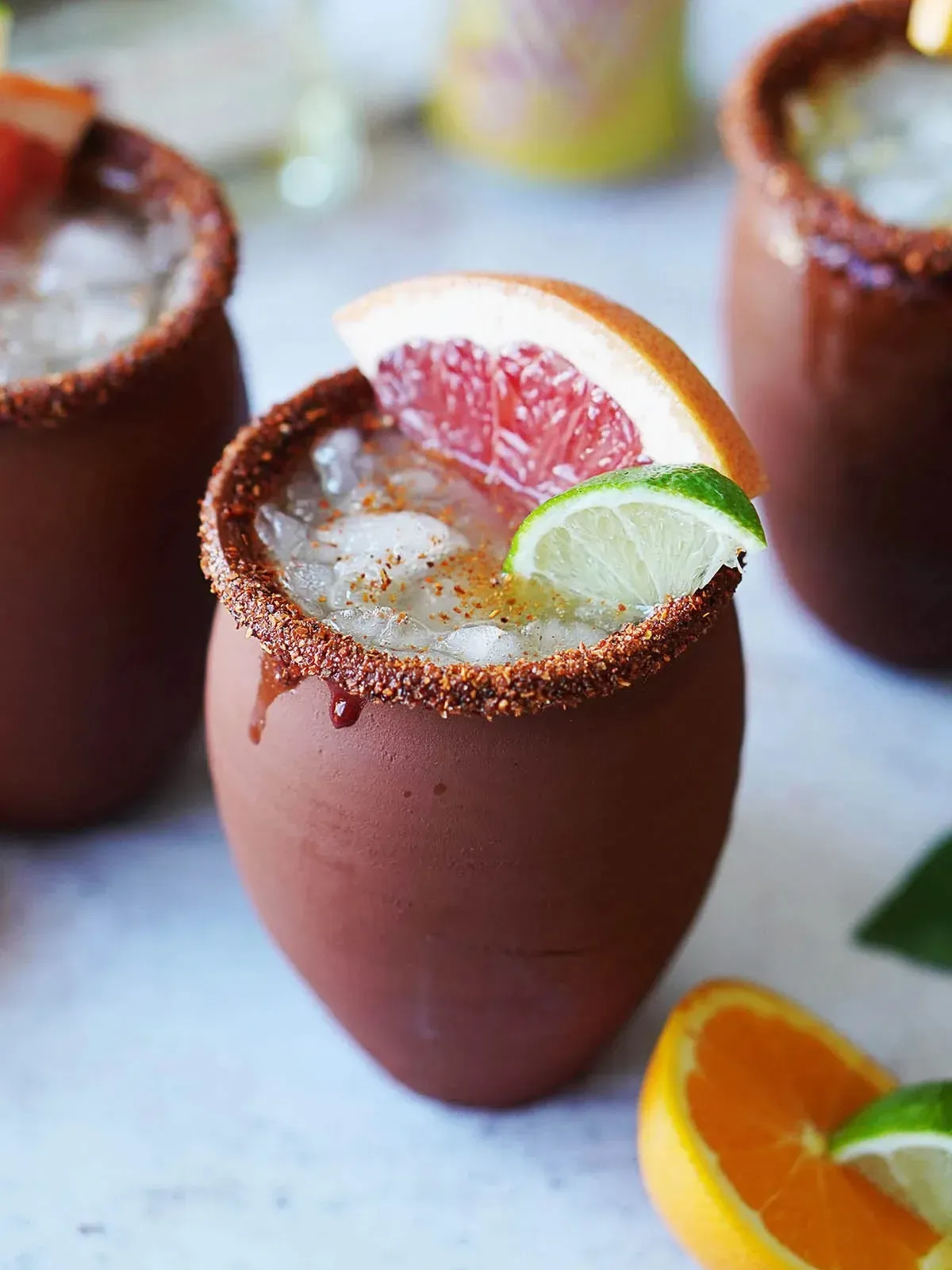Cocktails in terracotta mugs with ice, citrus garnishes, and a salted rim.