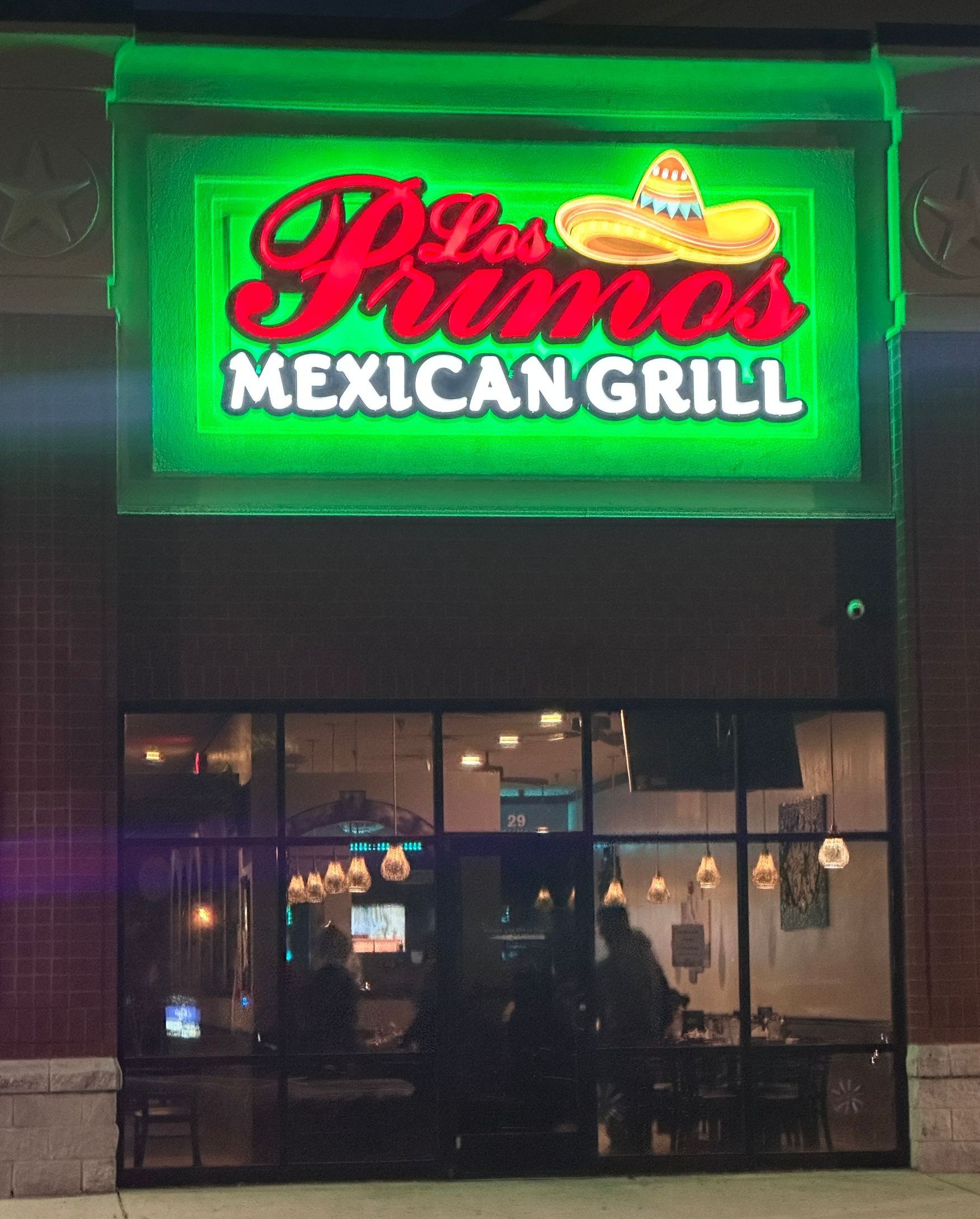 Los Pimos Mexican Grill restaurant front. Neon sign with green outline and sombrero graphic. People inside visible through glass windows.