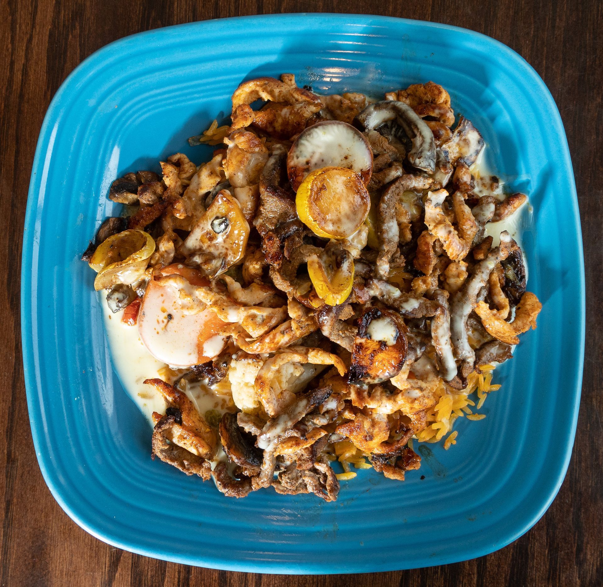Plate of food with fried onions, yellow squash, and sauce on a blue square plate.