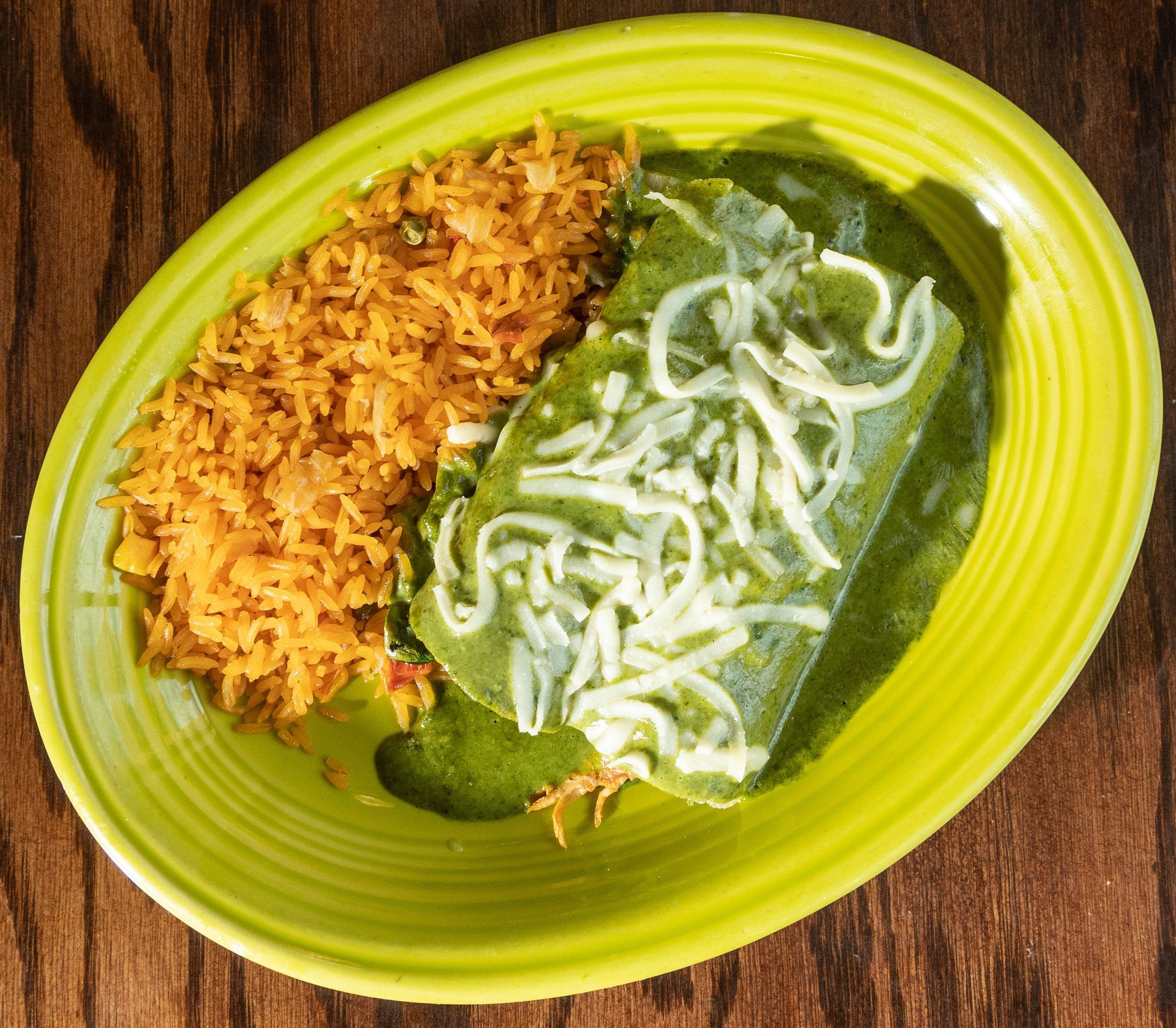 Green enchilada with cheese and rice on a yellow plate.