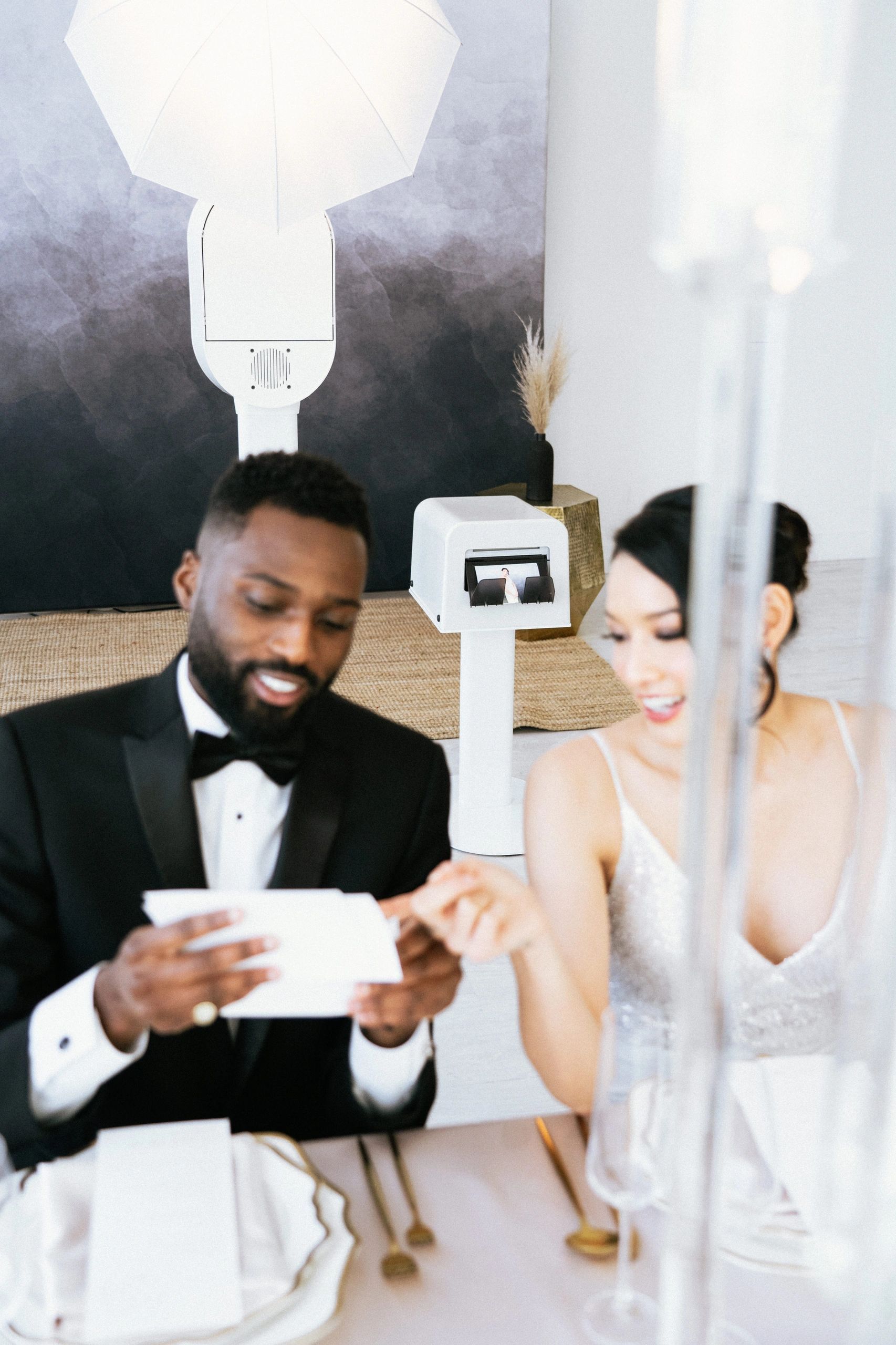 A bride and groom are sitting at a table looking at a card.