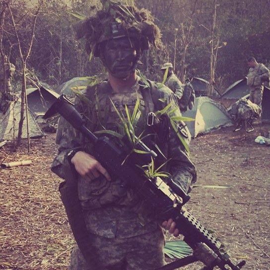 A soldier kneeling in the field with his rifle during a deployment