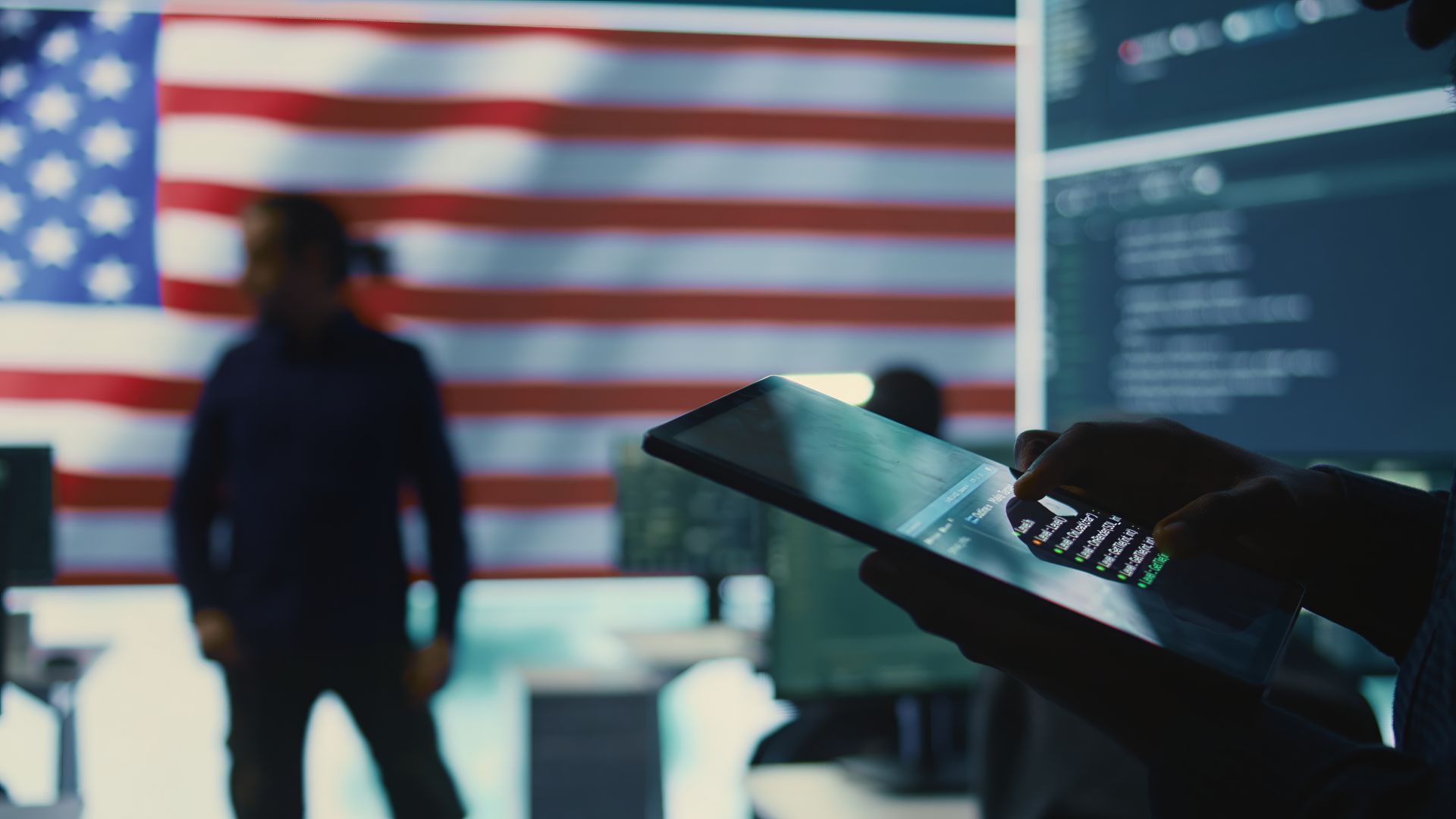 A veteran working at a bank of monitors in front of a large American flag