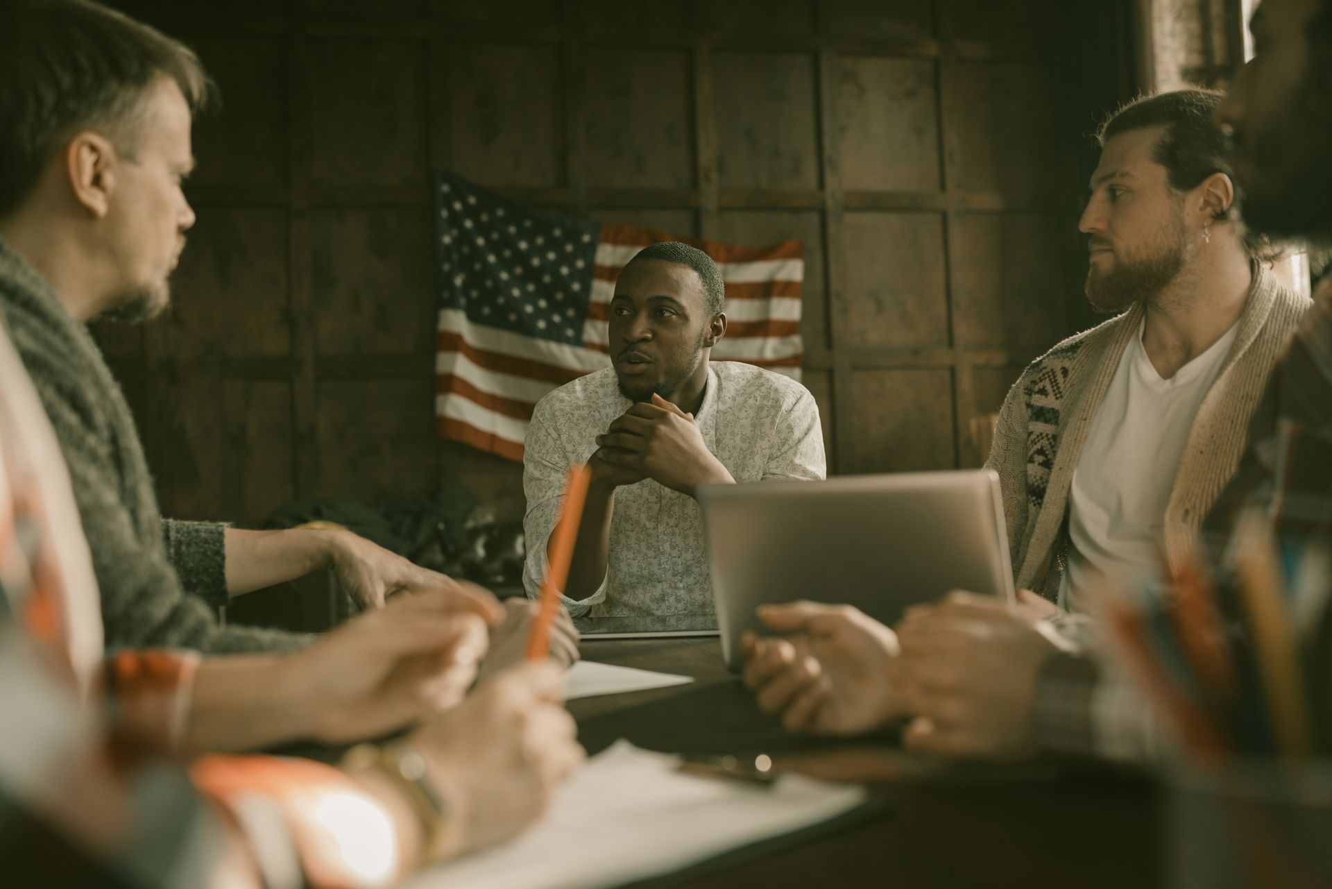 A veteran-owned business team meeting around a table with an American flag on the wall behind them