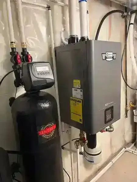 Water softener and gray HVAC control box in a basement with insulated walls and exposed pipes.