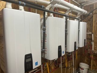 Row of white wall-mounted boilers and pipes in a utility room