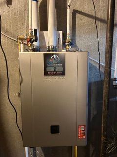 Gray HVAC furnace unit in a utility room with white vent pipes and a red inspection tag.