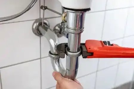 Hand tightening a chrome sink pipe with a red pipe wrench under a bathroom sink