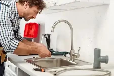 Man repairing a kitchen faucet beside a sink with tools on the counter