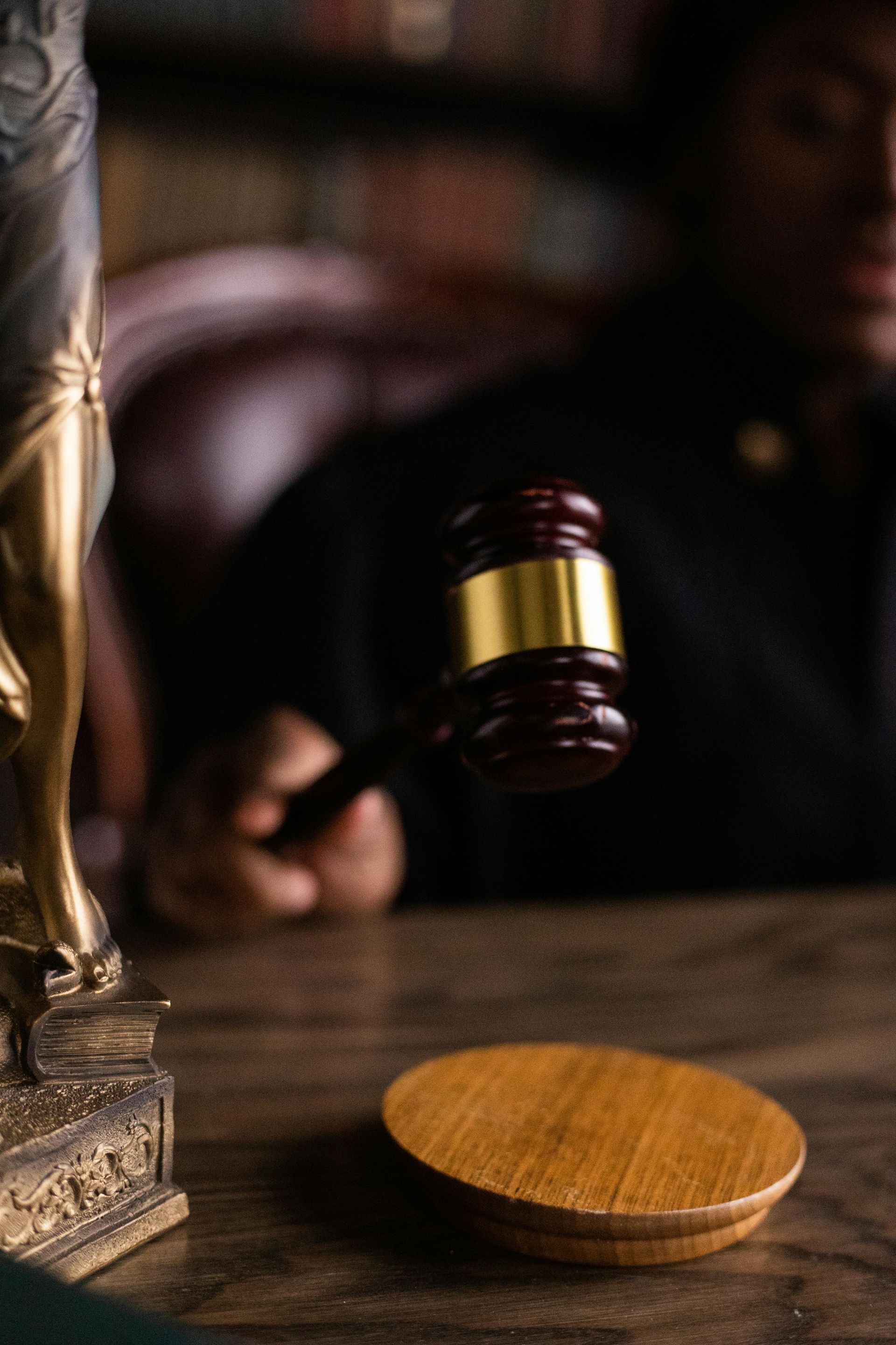 Gavel over wooden block on a desk in a courtroom setting, with a statue of justice in the background.