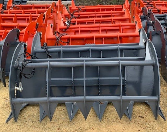 Gray and orange grapple buckets with tines, ready for use, outdoors.