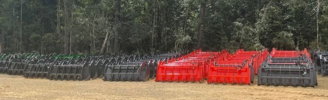 Rows of dumpsters, some red, some black, arranged on grassy field with trees in background.