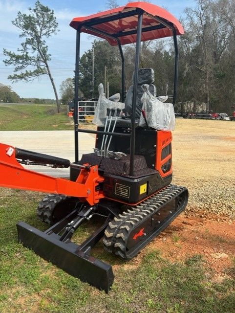 Orange and black mini excavator with canopy, on tracks, parked outdoors.