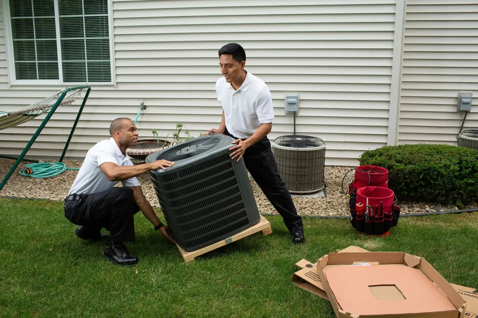 Two men are installing an air conditioner in a backyard.