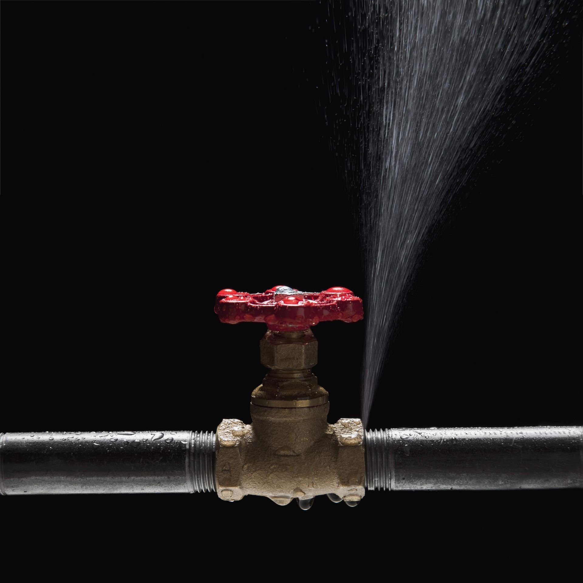 Water is spraying from a leaking pipe valve with a red handle. Water is spraying from a leaking pipe valve with a red handle.