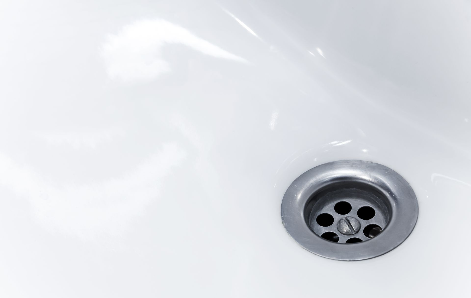 Close-up of a white sink with a circular, metal drain.