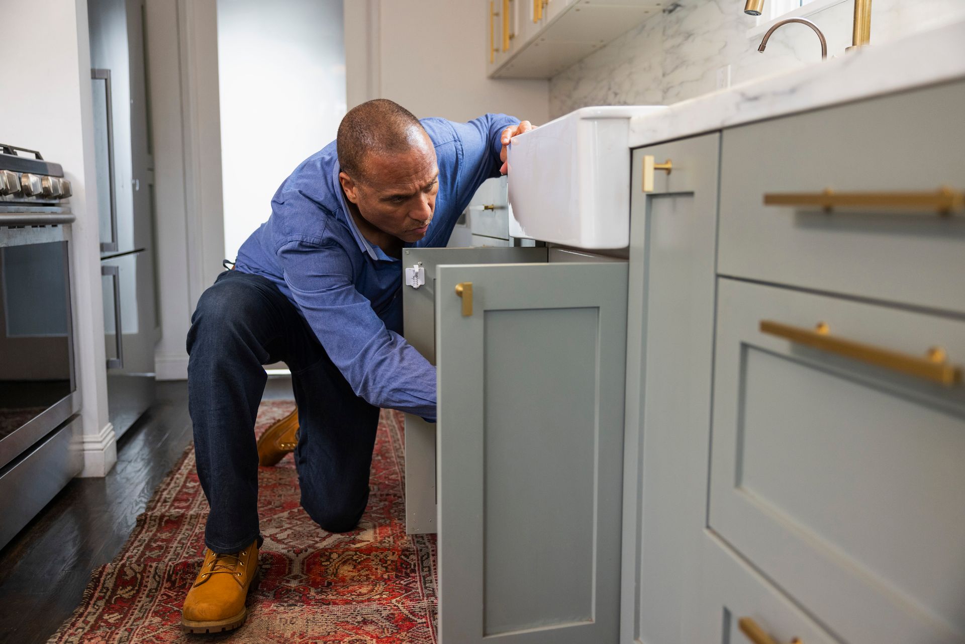 Plumber repairing kitchen sink pipes inside cabinet of modern white and gray kitchen.