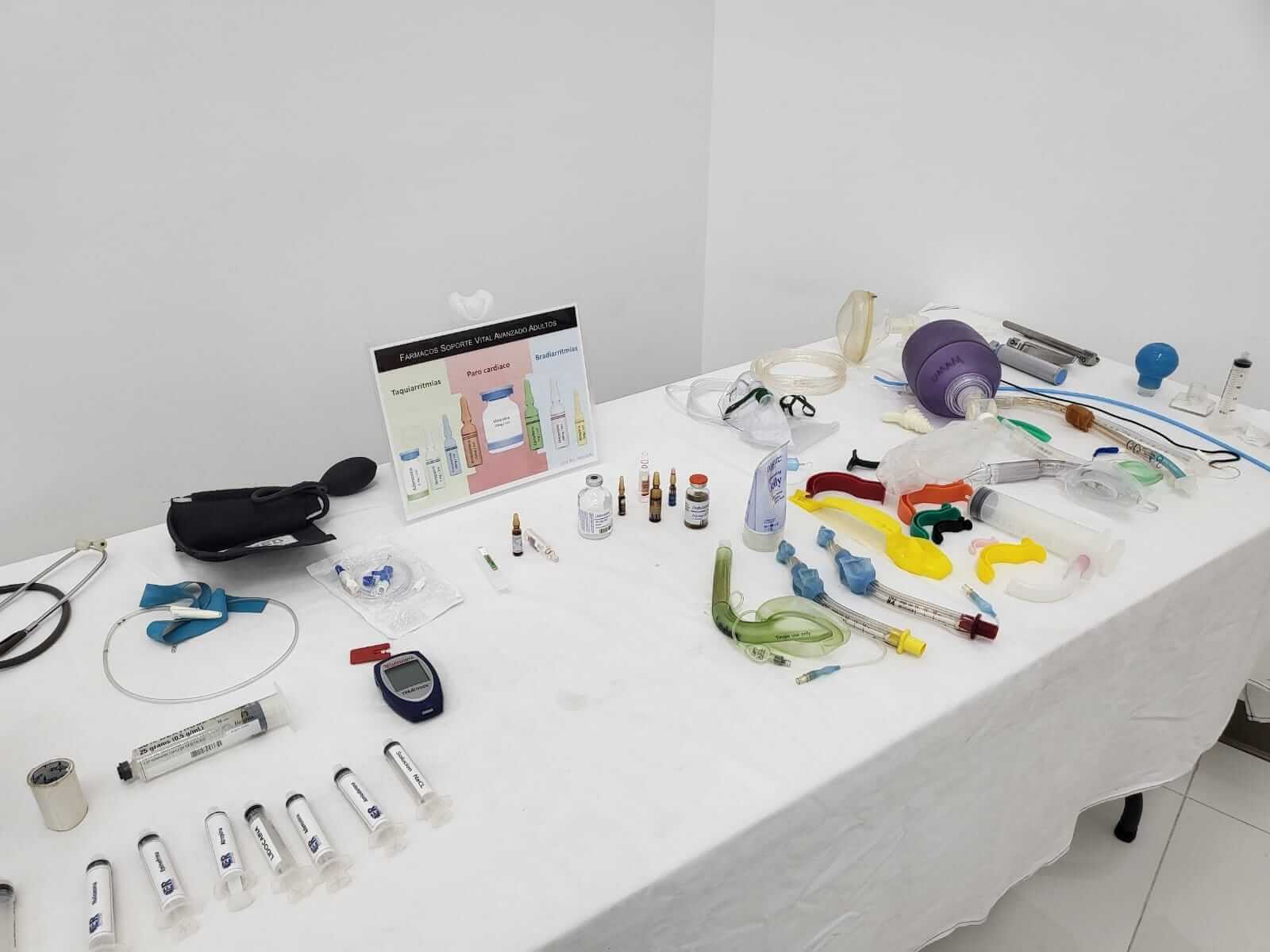 Equipo médico dispuesto sobre una mesa blanca: jeringas, suministros para las vías respiratorias y un monitor.