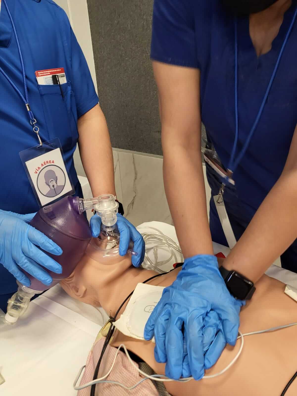 Dos personas con uniformes azules que utilizan una máscara con válvula de bolsa en un maniquí para proporcionar respiraciones de rescate.