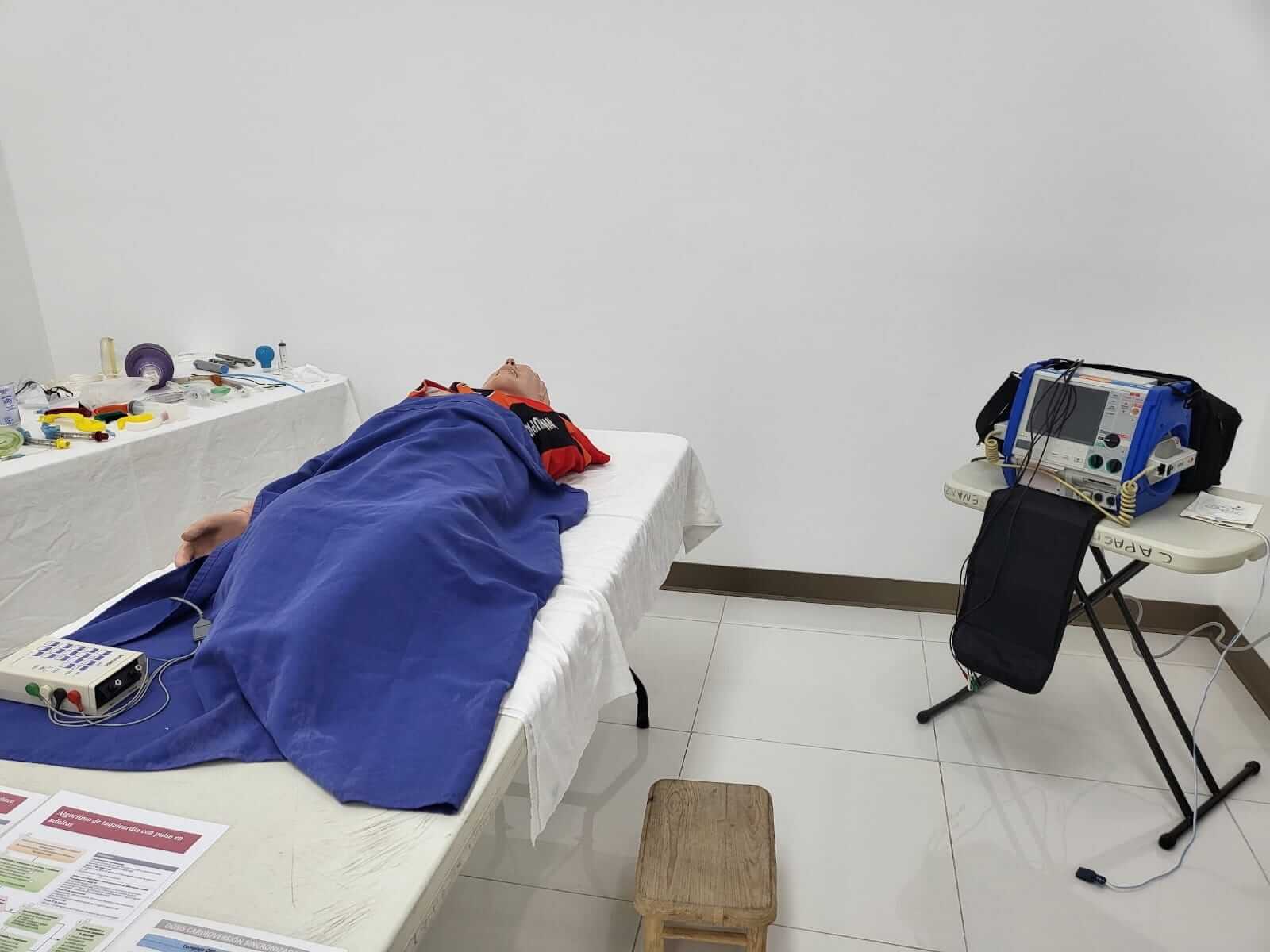 Un maniquí médico acostado en una cama con equipo. Se ven un respirador y un dispositivo de monitorización.