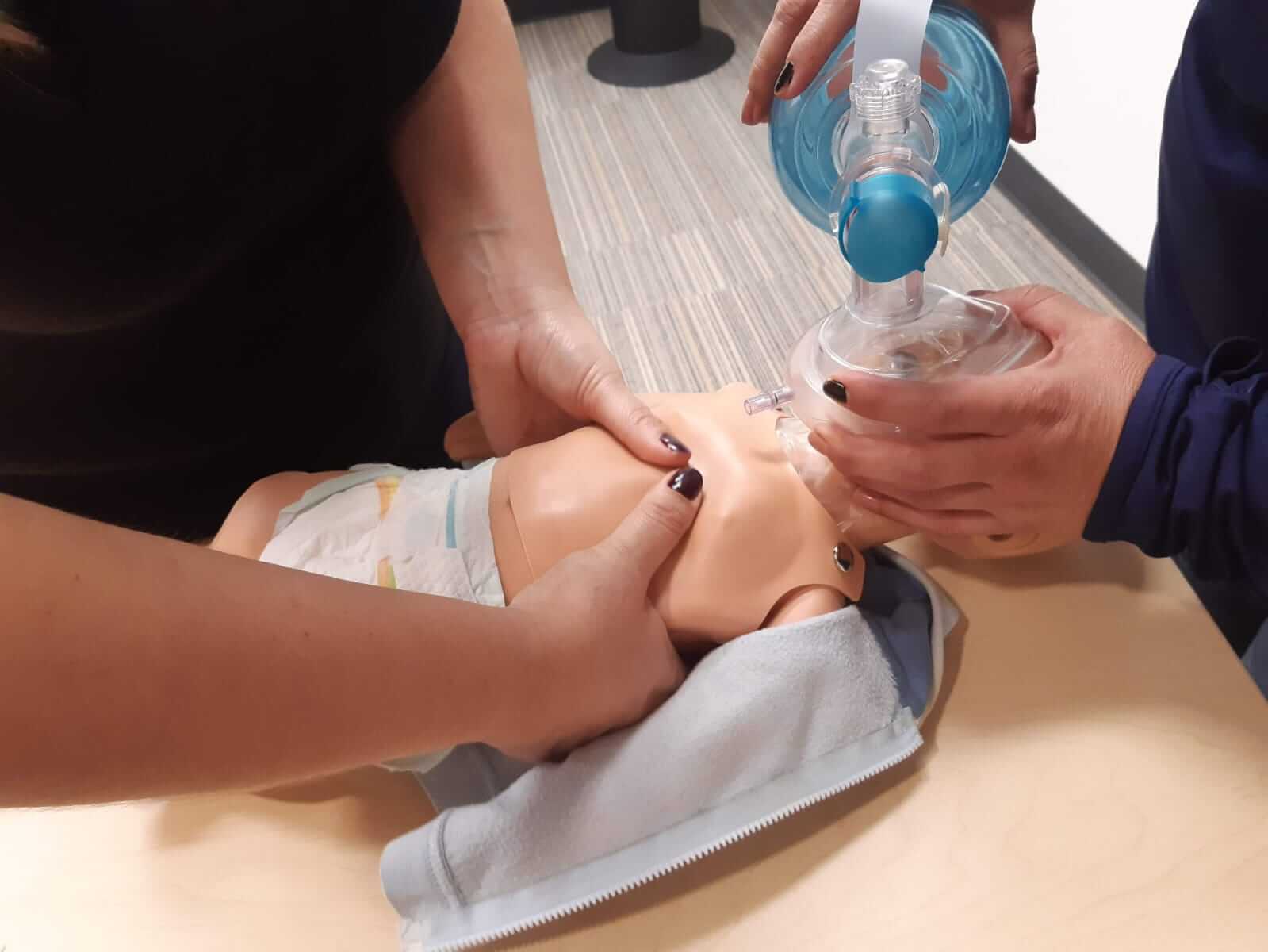 Tres personas practican el uso de una máscara con válvula de bolsa en un maniquí del tamaño de un bebé.