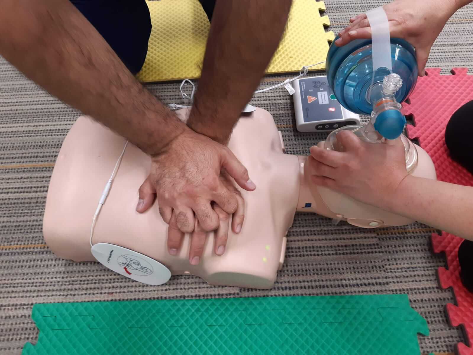 Dos personas practicando RCP en un maniquí, una administrando compresiones torácicas y la otra con una máscara de respiración.