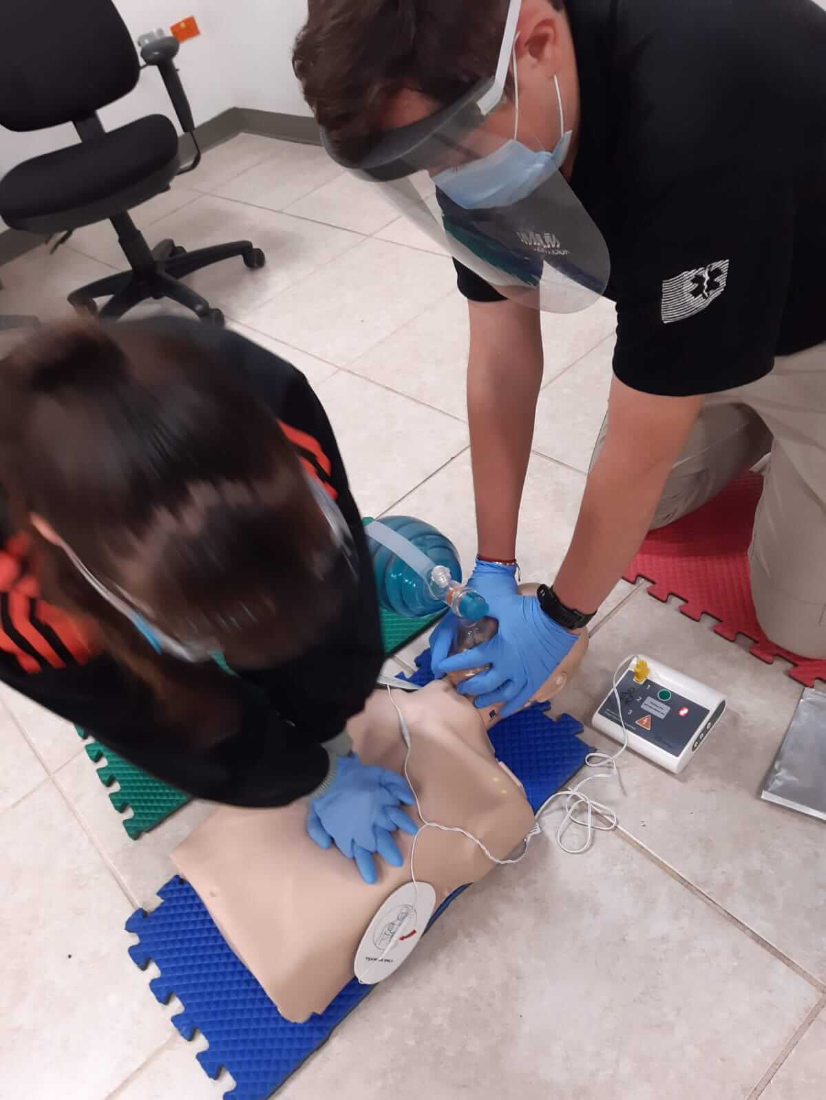 Dos personas practican RCP en un maniquí, con máscaras y guantes; DEA cerca.