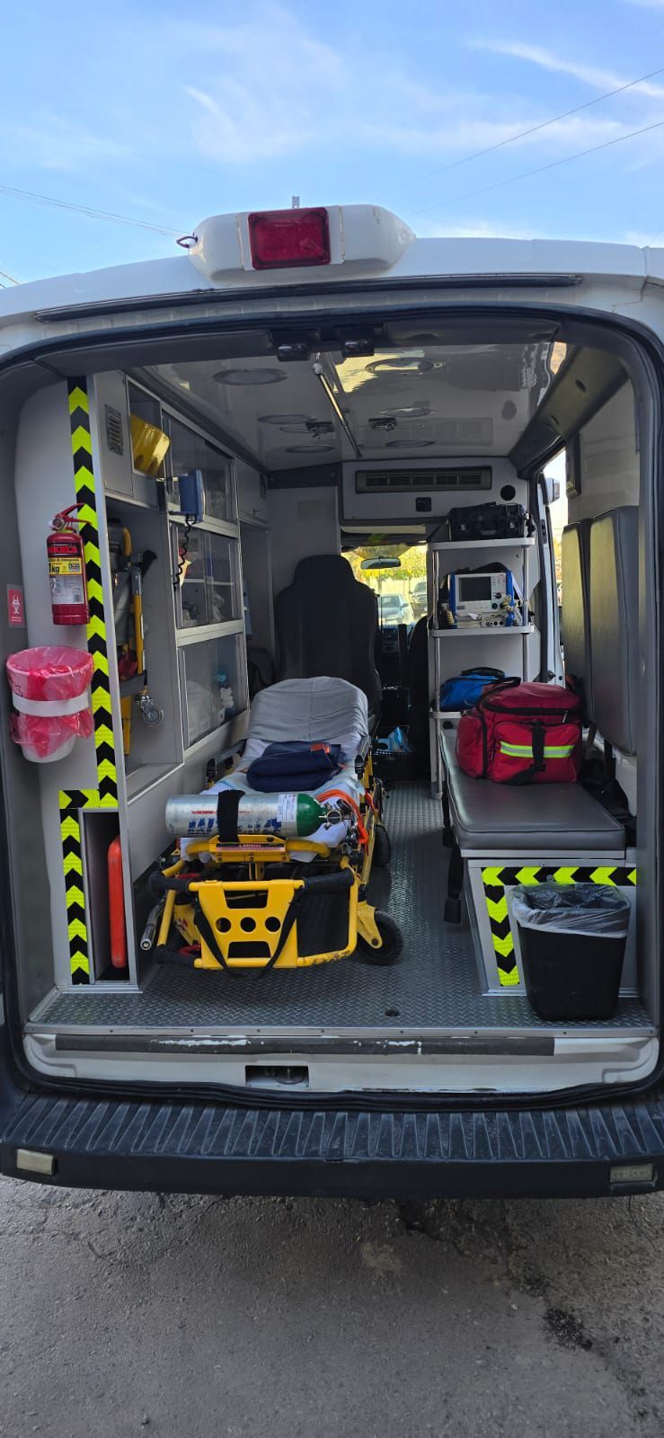Interior de una ambulancia con equipo médico, una camilla y compartimentos de almacenamiento. Se aprecian marcas de seguridad negras y amarillas.
