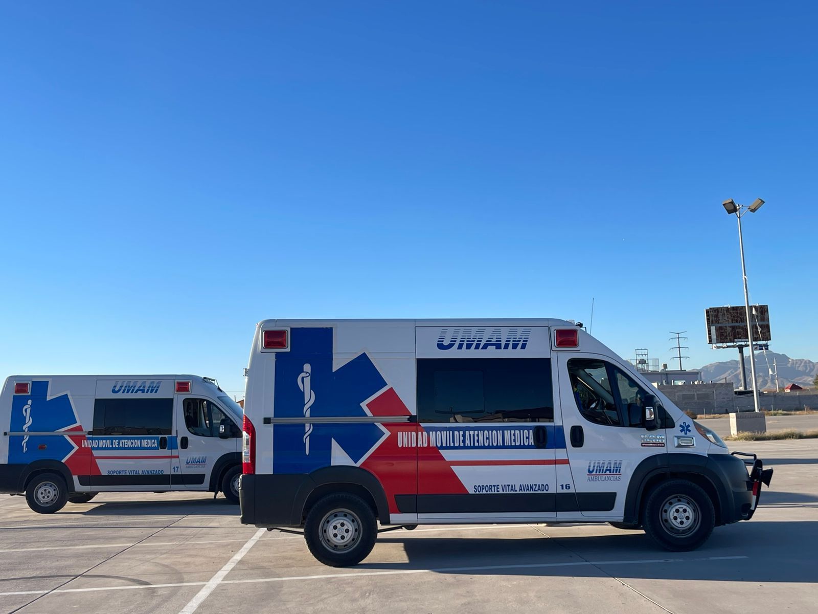 Dos ambulancias blancas y azules estacionadas al aire libre en un día soleado.