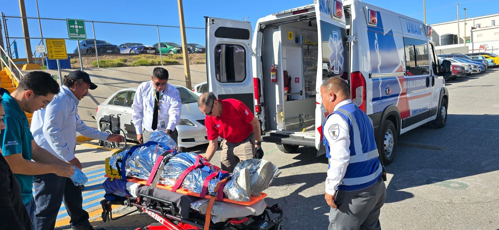 Personal médico carga a un paciente, cubierto con una manta térmica, en una ambulancia.