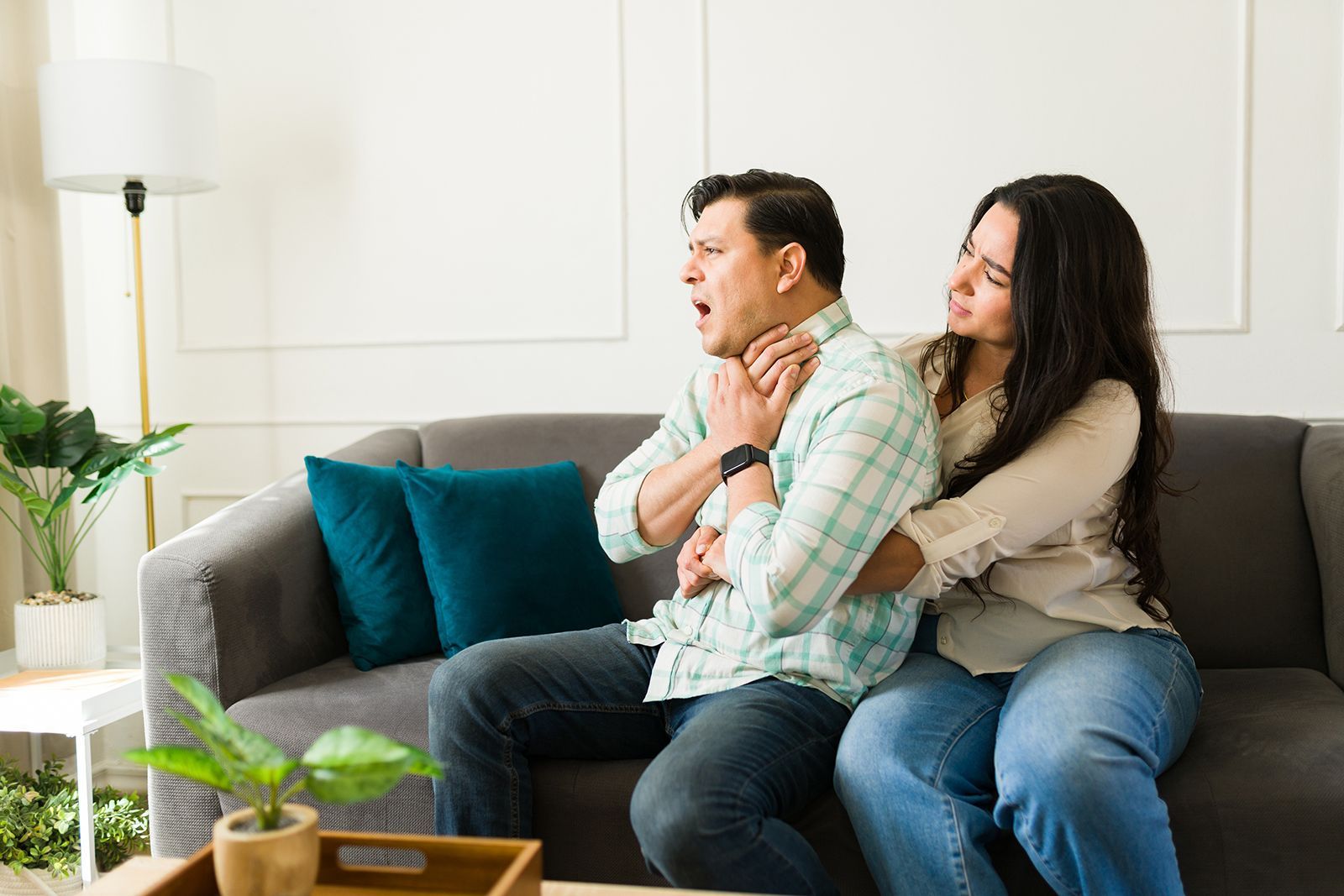 Mujer realizando la maniobra de Heimlich a un hombre sentado en un sofá.