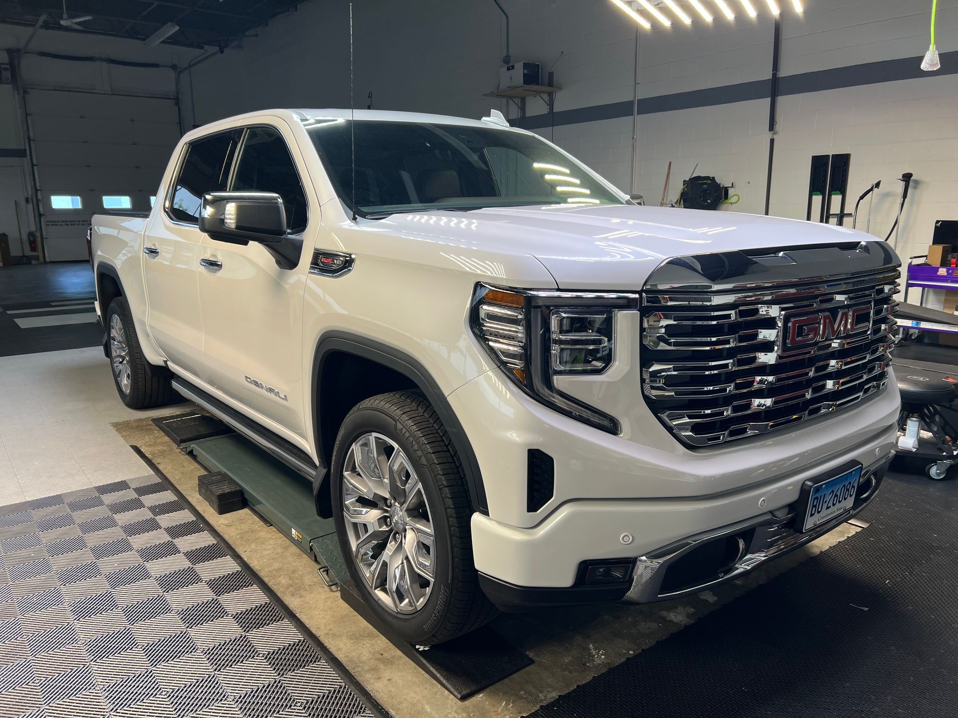 White GMC Sierra pickup truck in a garage, chrome accents, shiny wheels.