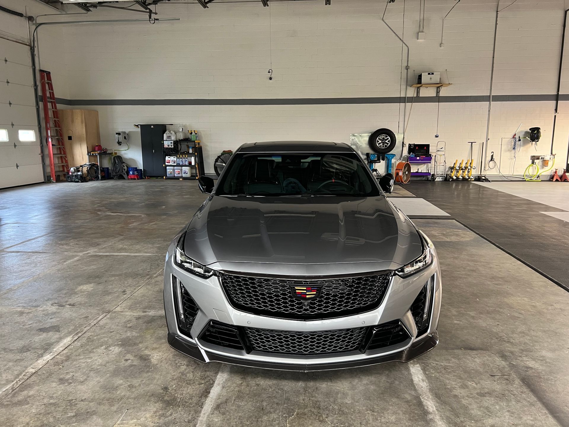 Silver Cadillac sports car inside a garage. Black grille, black roof, concrete floor.