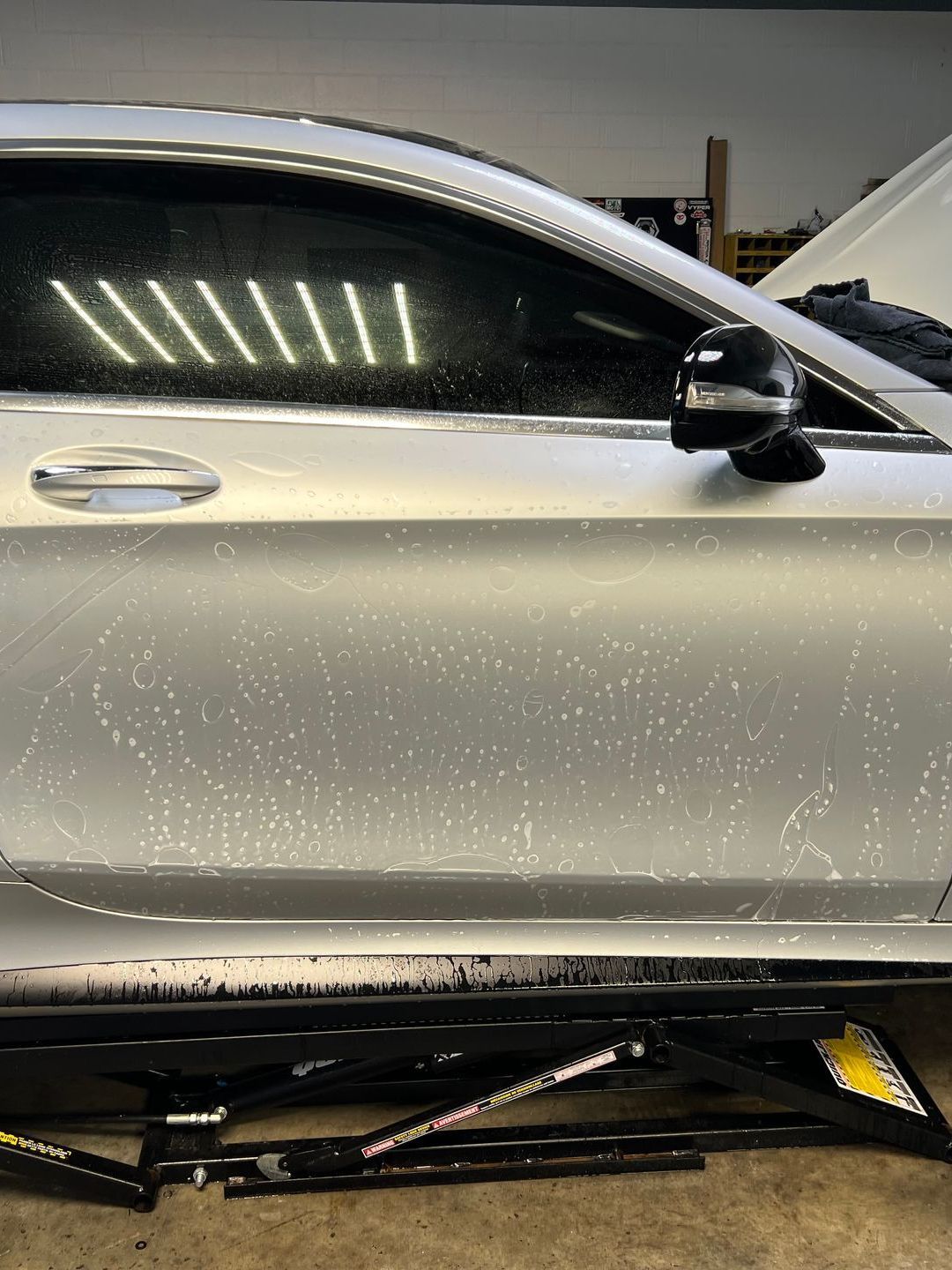 A silver car is parked on a lift in a garage.