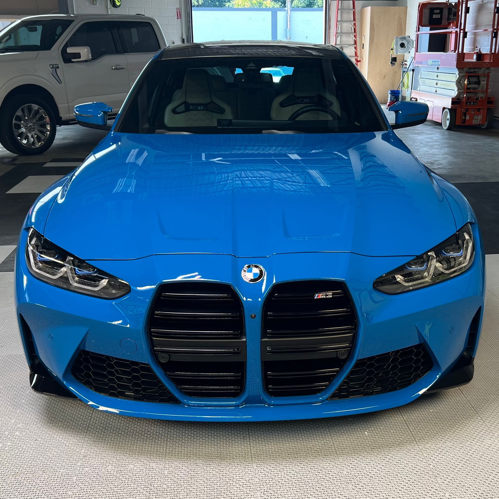 A blue bmw is parked in a garage next to a white truck.