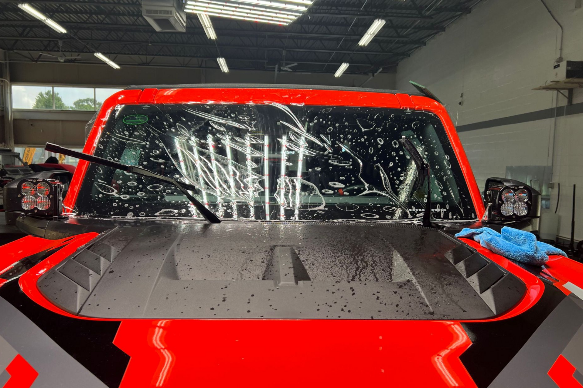 Red truck getting a window film applied in a garage.