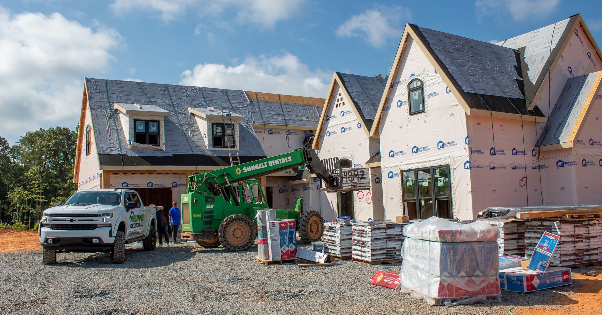 Construction site, house under construction. A forklift unloads materials. A pickup truck is parked nearby.