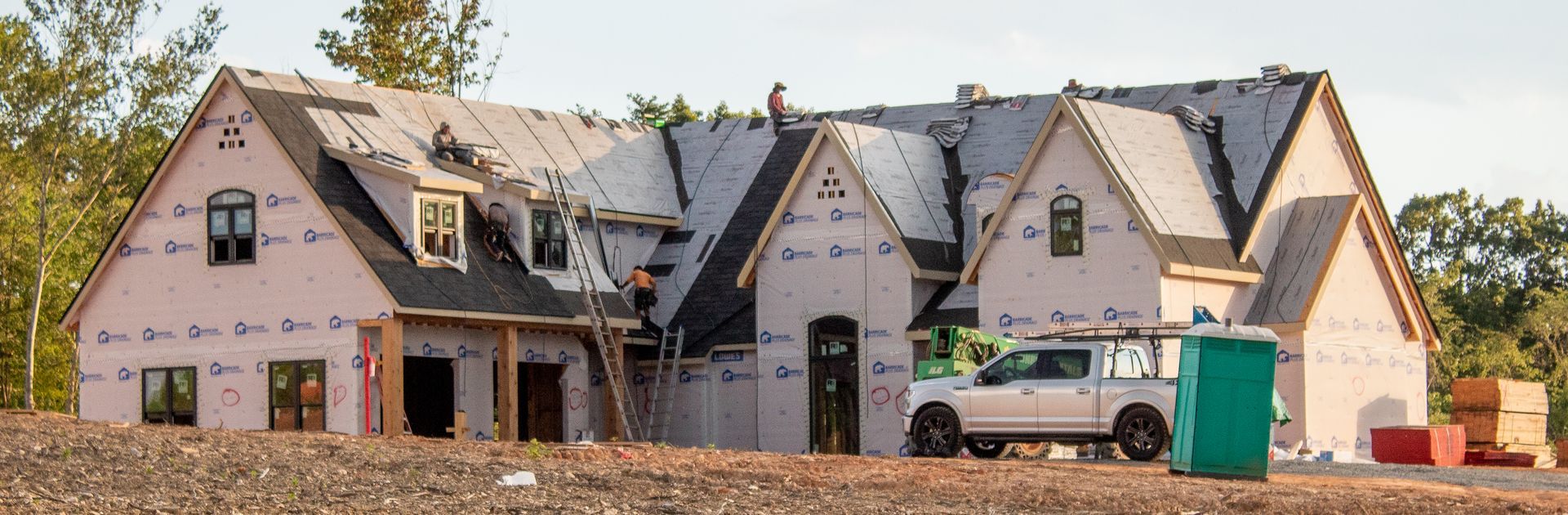 House under construction, with roof partially complete and a pickup truck parked nearby.