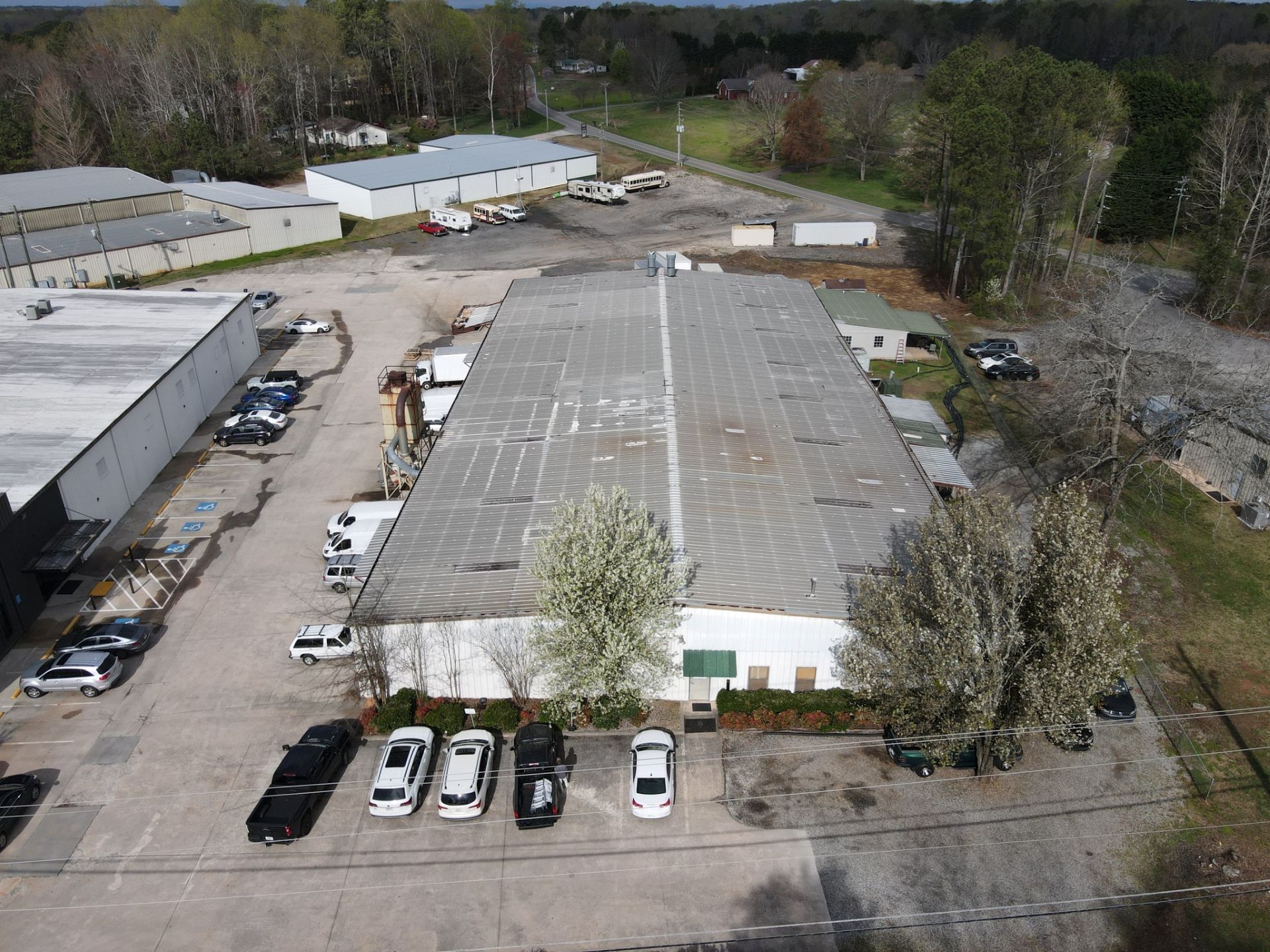 Aerial view of industrial buildings with cars, trucks, and trees on a sunny day.