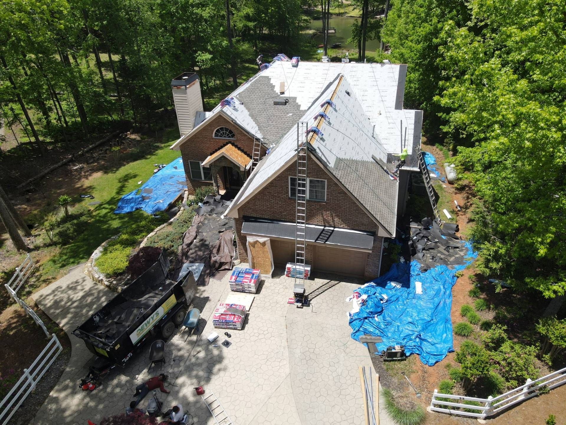 House under roof renovation, with a dumpster, materials, and tarps on the driveway.