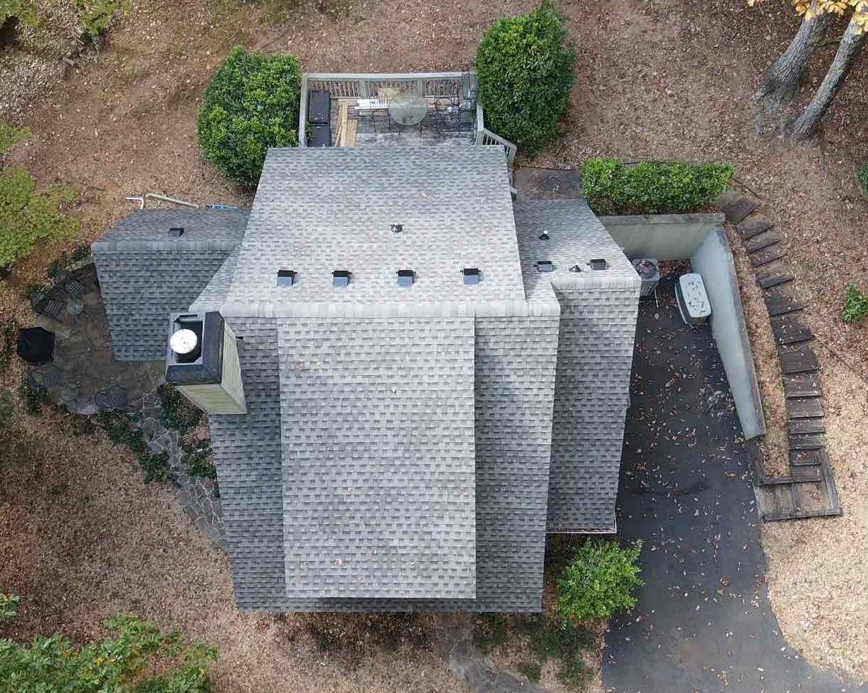 Aerial view of a gray-roofed house with landscaping and a chimney.