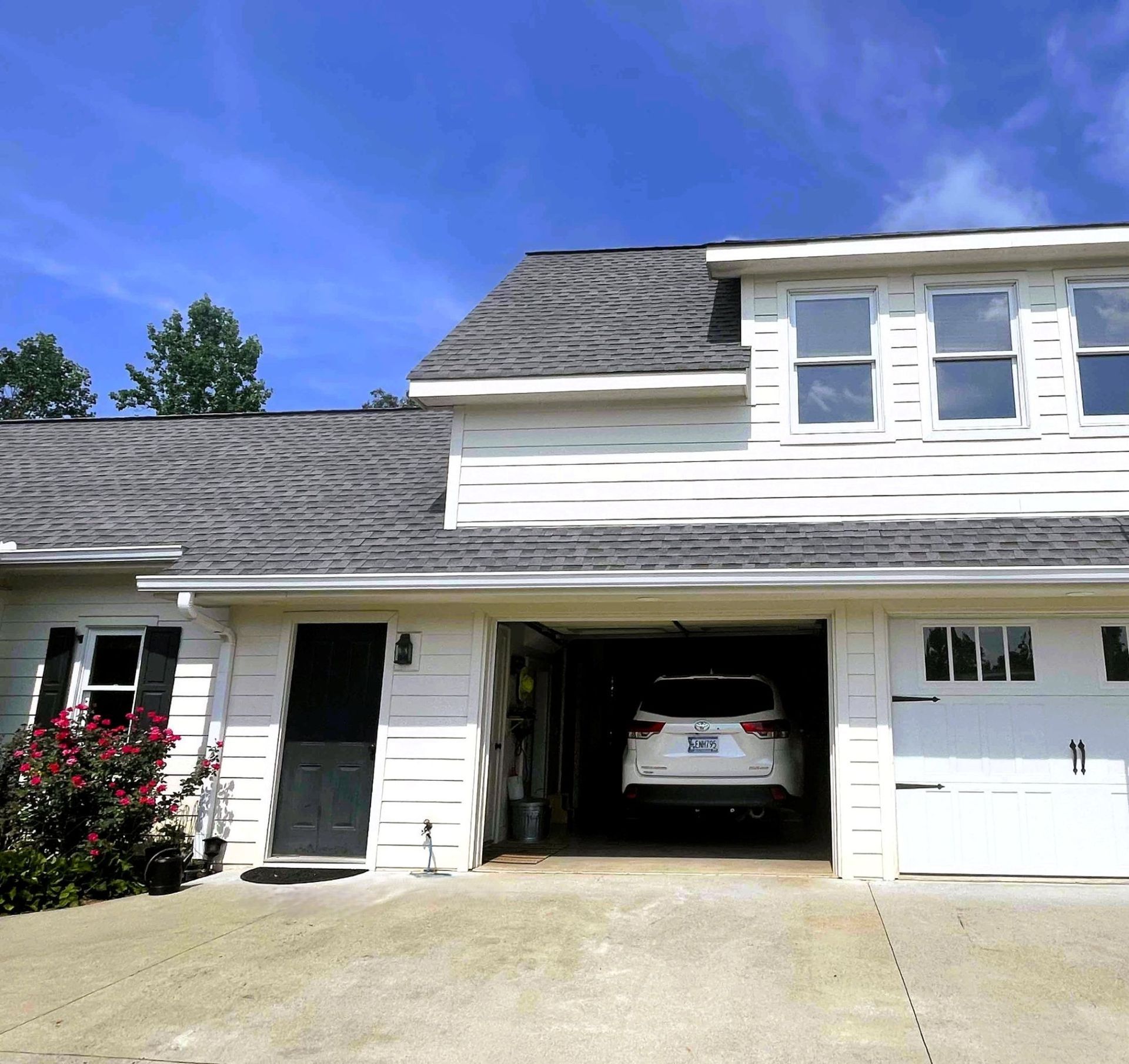 White house with gray roof, attached garage with white SUV, and blue sky.